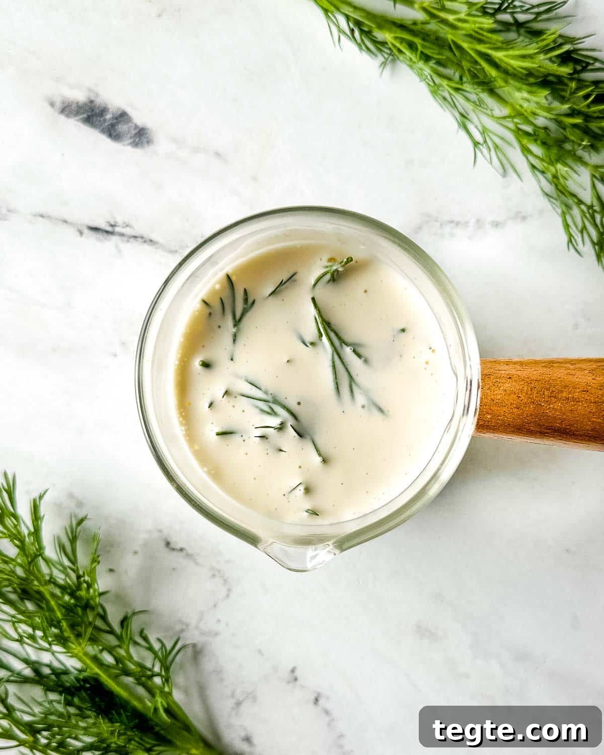 Creamy Dill Sauce for Fish, Salmon, and Vegetables 2 closeup of dill sauce in a glass container with a wooden handle on a white marble counter.