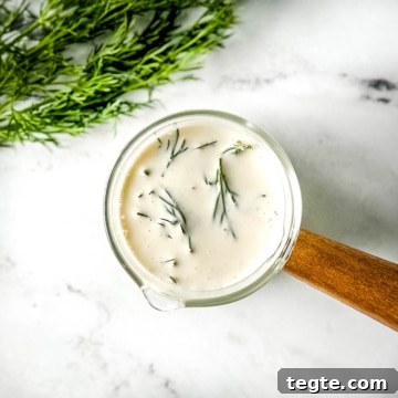 Creamy Dill Sauce for Fish, Salmon, and Vegetables 7 closeup of dill sauce in a glass container with a wooden handle on a white marble counter.