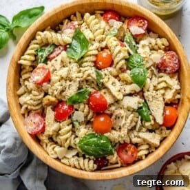 Over 20 St. Patrick’s Day Recipes for Festive Celebrations 20 pesto pasta in a round bowl with tomatoes, chicken, basil garnish.