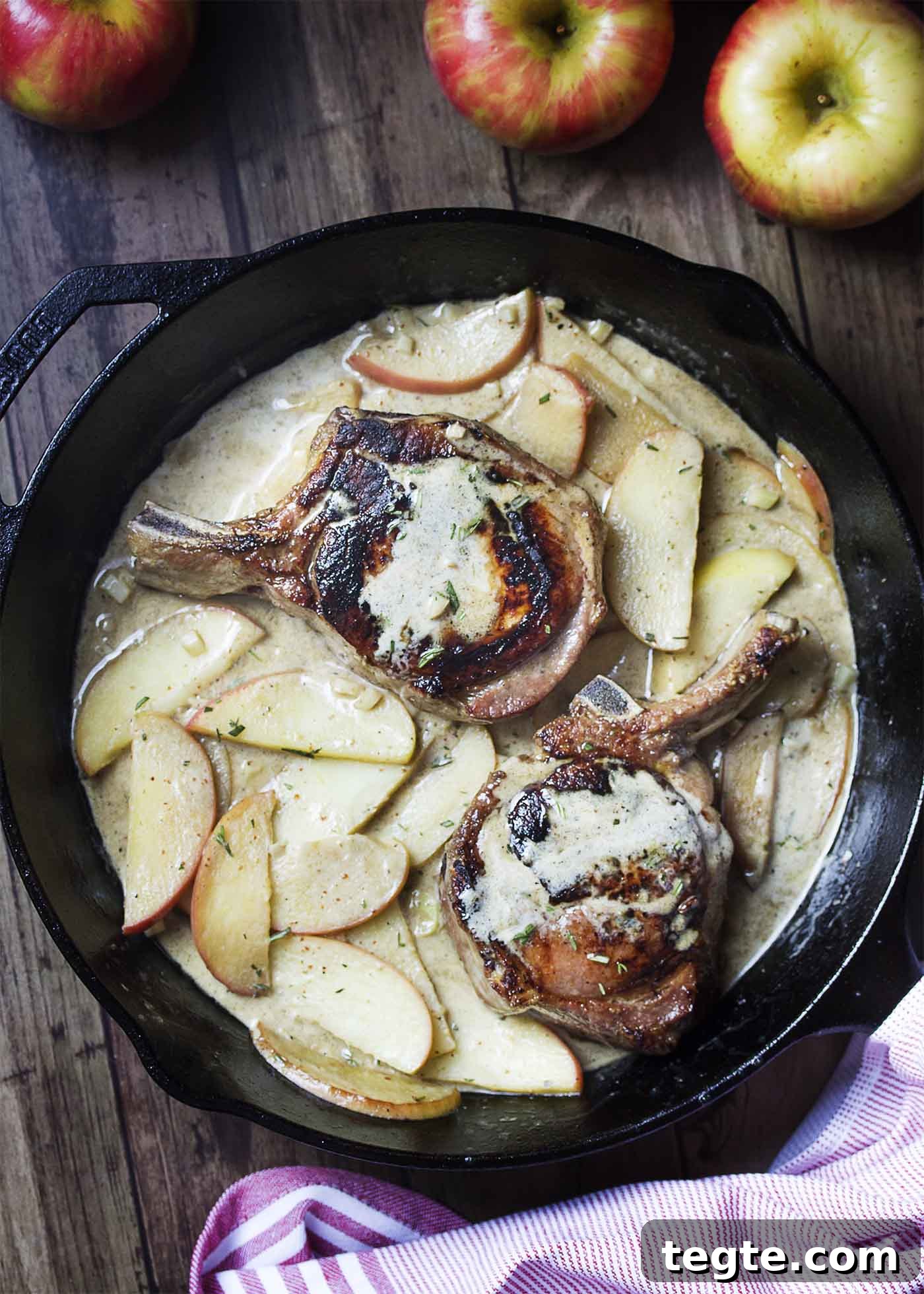 Two seared chops in a cast iron skillet surrounded by apple cream sauce.