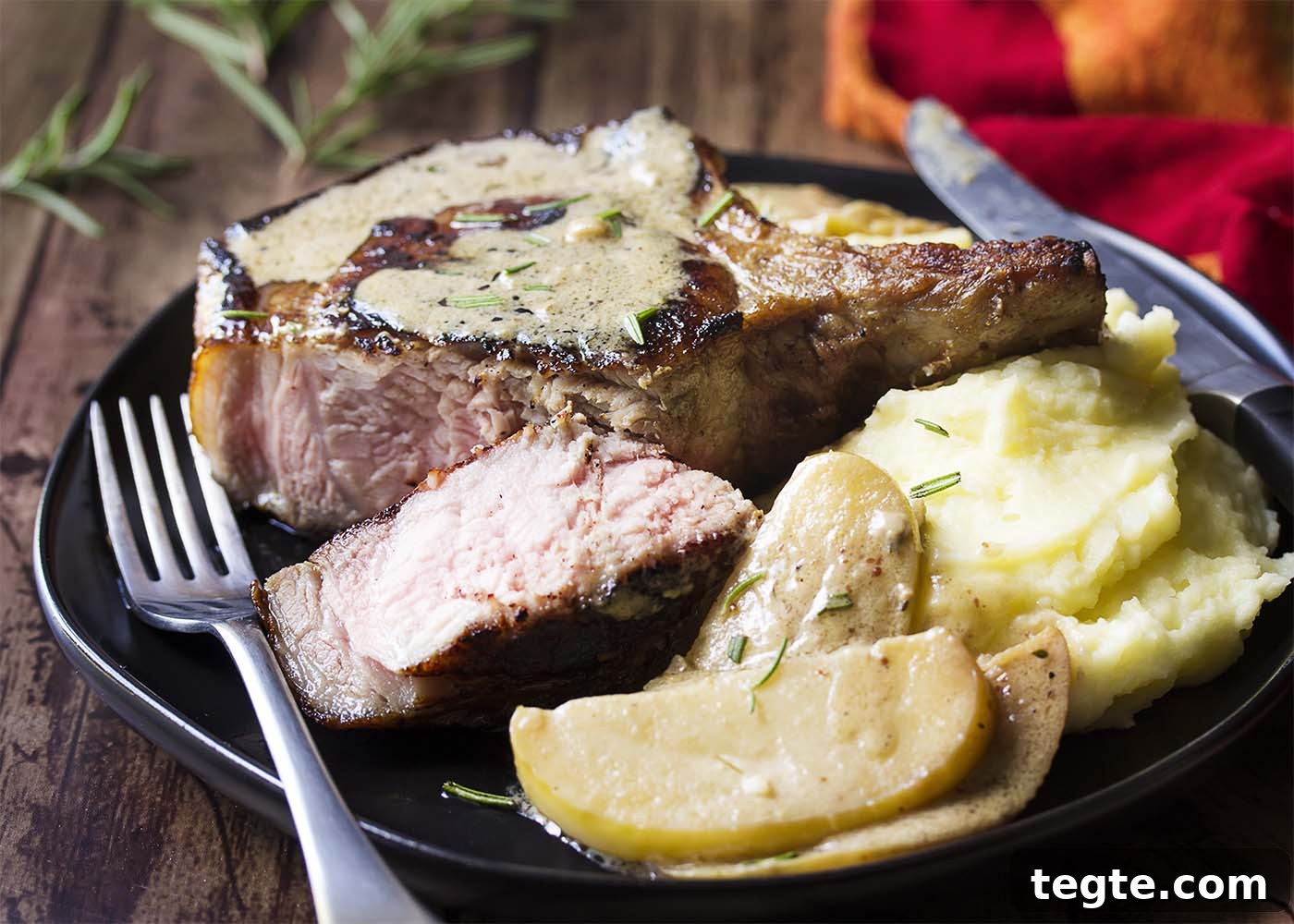 Thick pork chop cut open showing the juicy pink interior all on a black plate.