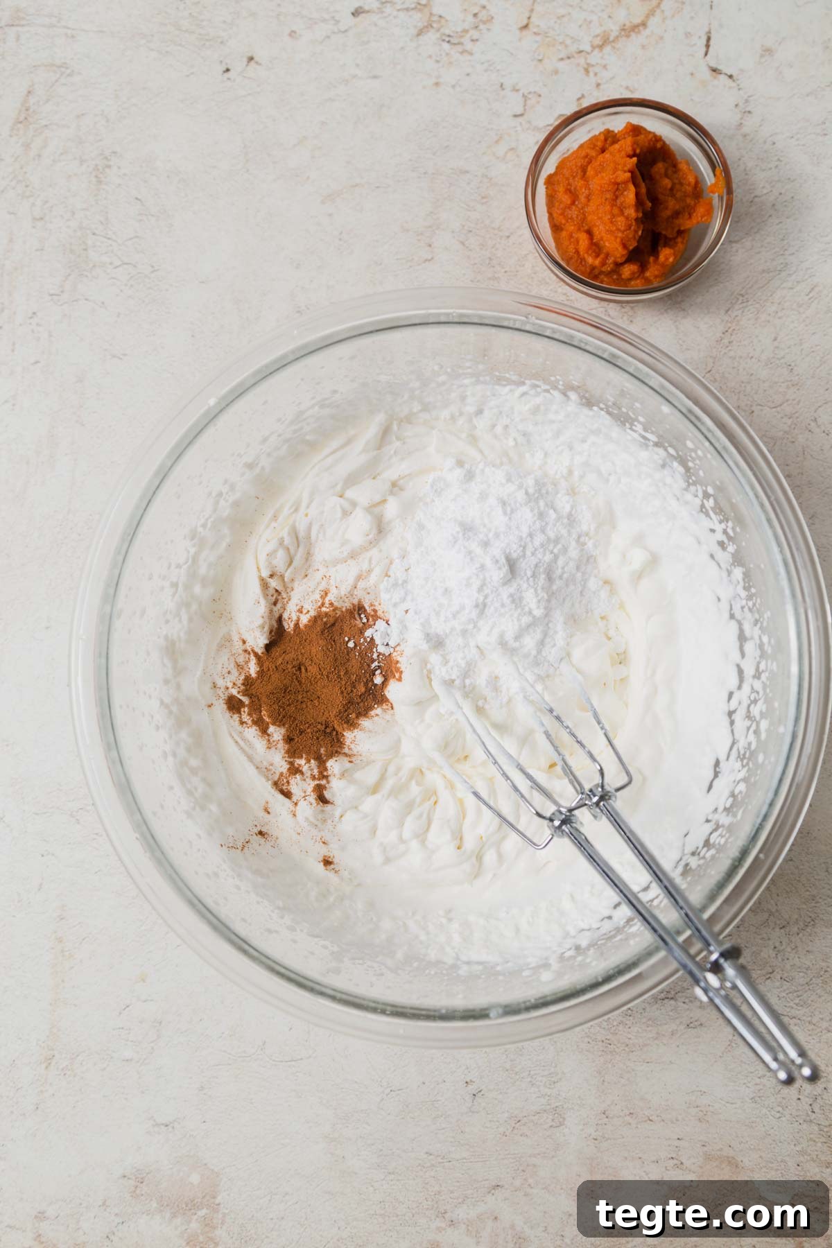 Pumpkin-Spiced Whipped Cream Recipe for Fall Desserts 5 pumpkin whipped cream with pie spice and sugar in a bowl.