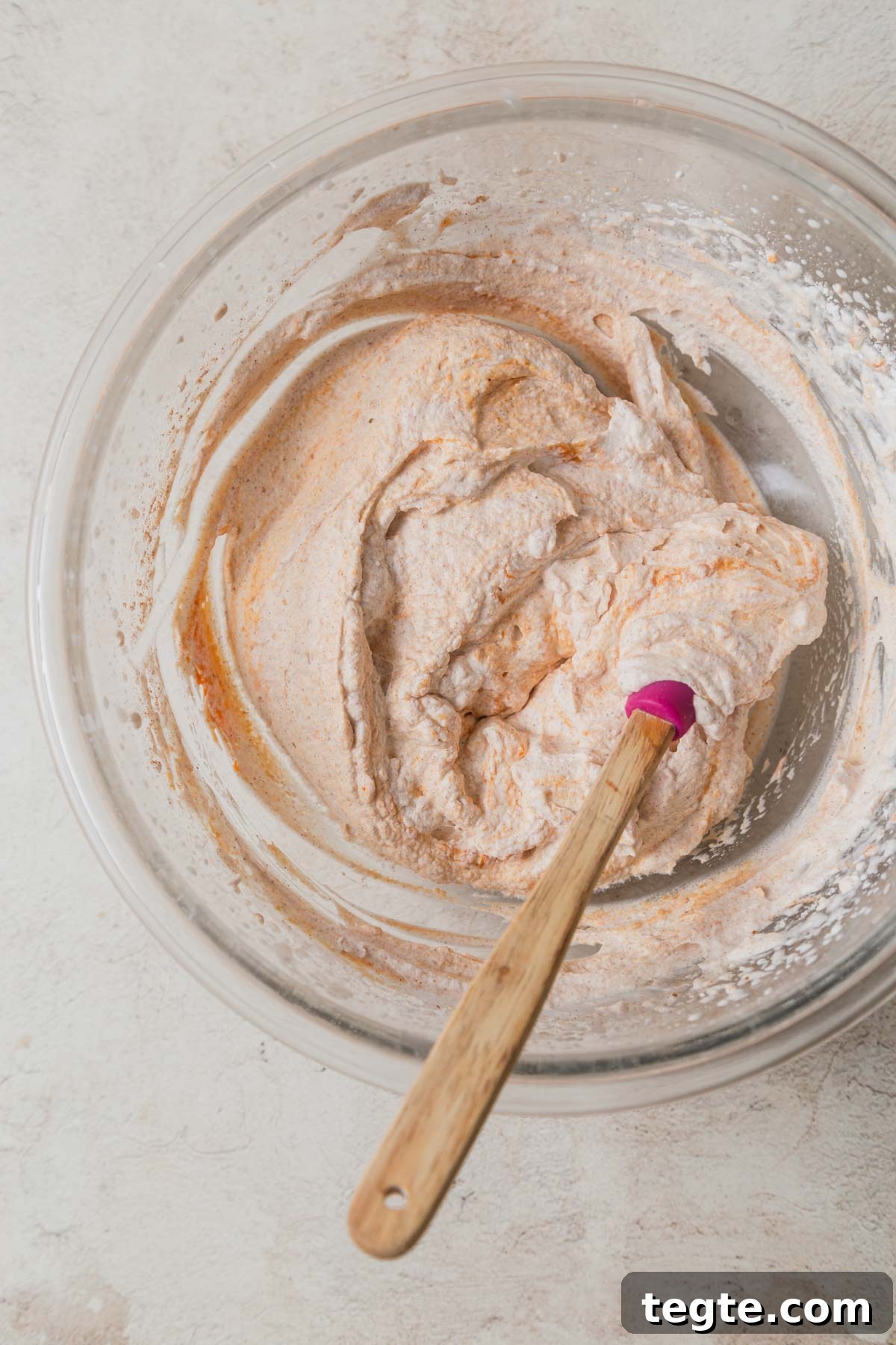 Pumpkin-Spiced Whipped Cream Recipe for Fall Desserts 7 pumpkin whipped cream in a bowl with a spatula.