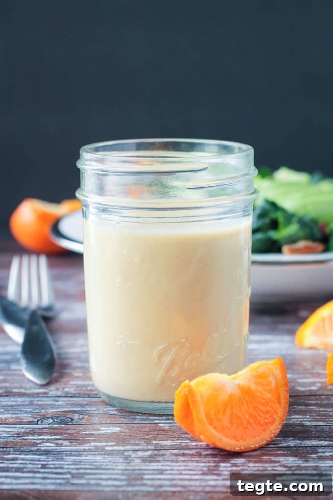 Citrus Tahini Dressing - this creamy, oil-free dressing is the perfect drizzle for all of your leafy greens. Fresh squeezed orange juice for sweetness and apple cider vinegar for tang combine with the creamy tahini for the perfect flavor balance. Jar of citrus tahini dressing w/ an orange slice in front of the jar.
