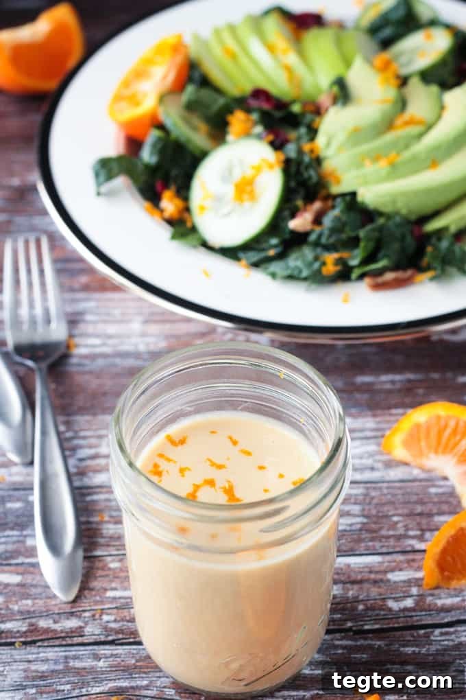 Citrus Tahini Dressing - this creamy, oil-free dressing is the perfect drizzle for all of your leafy greens. Fresh squeezed orange juice for sweetness and apple cider vinegar for tang combine with the creamy tahini for the perfect flavor balance. Jar of sauce in front of a kale salad.