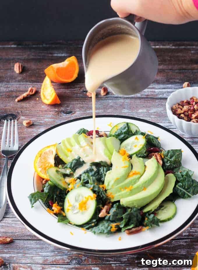 Citrus Tahini Dressing - this creamy, oil-free dressing is the perfect drizzle for all of your leafy greens. Fresh squeezed orange juice for sweetness and apple cider vinegar for tang combine with the creamy tahini for the perfect flavor balance. Orange Tahini Dressing being poured onto a lacinato kale salad.