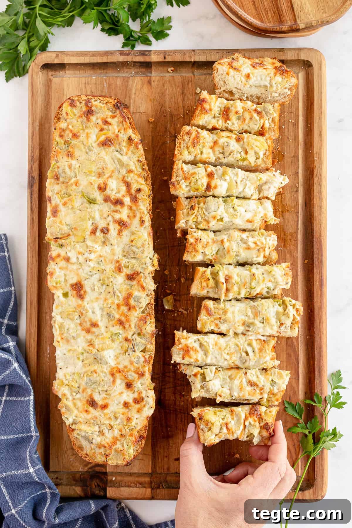 Cheesy Artichoke Pull-Apart Bread for Parties and Snacks 2 A hand reaching for a slice of Cheesy Artichoke Bread on a cutting board.