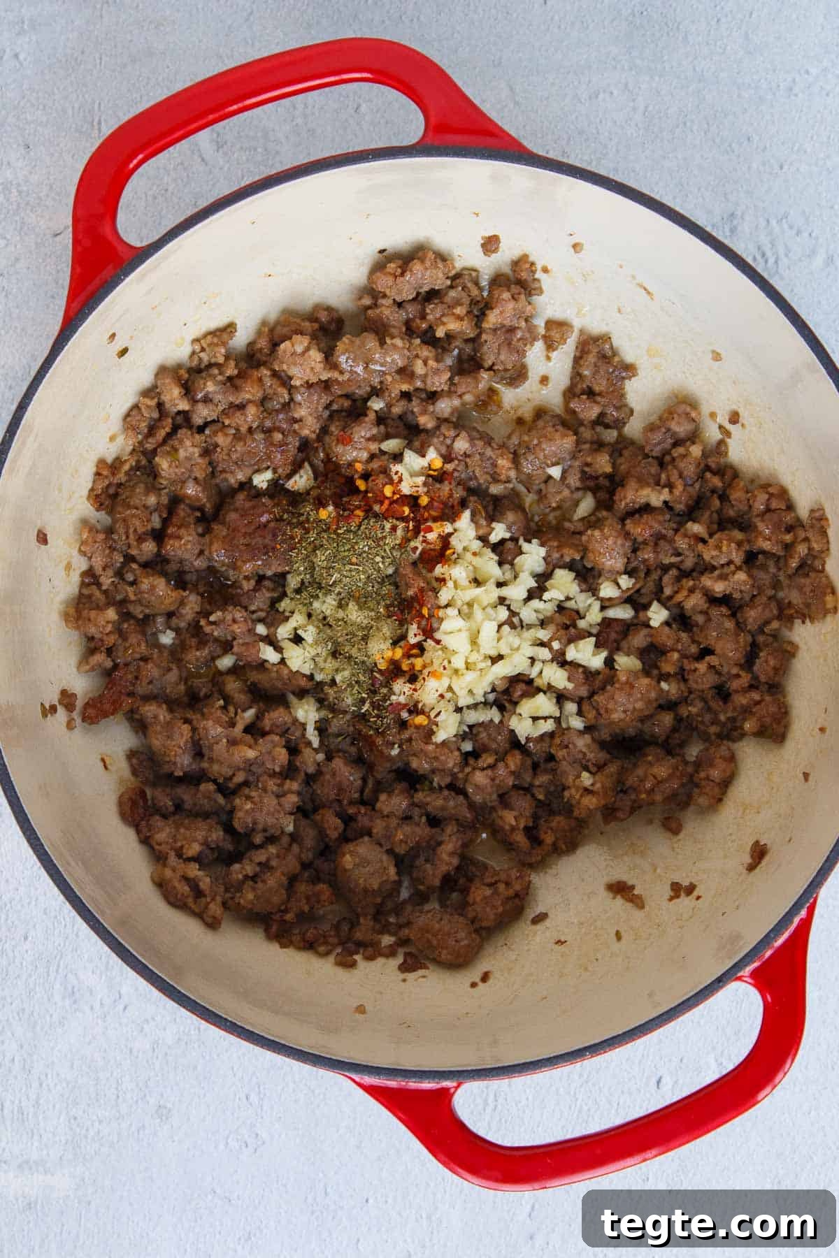 Garlic, Italian seasoning, and red pepper flakes added to cooked Italian sausage in a large pot