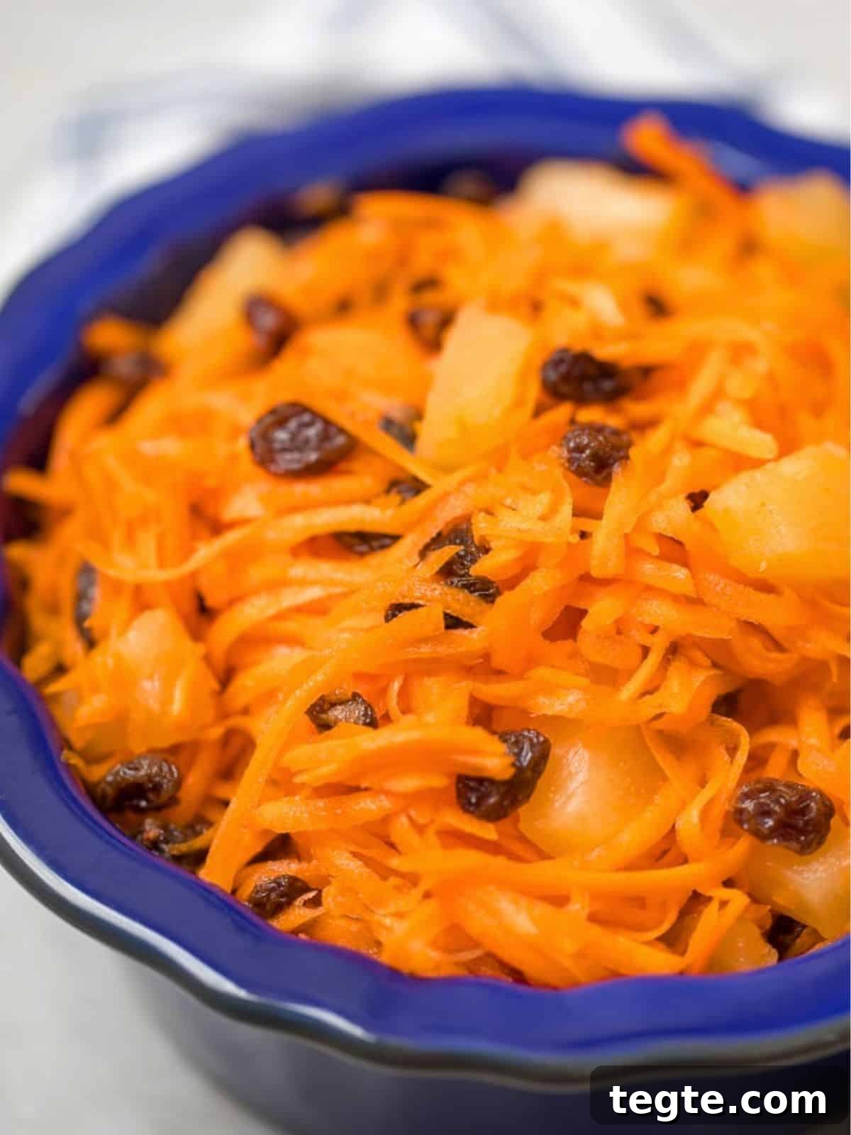 Carrot Raisin Salad Shredded carrot salad with raisins and pineapple in blue bowl.