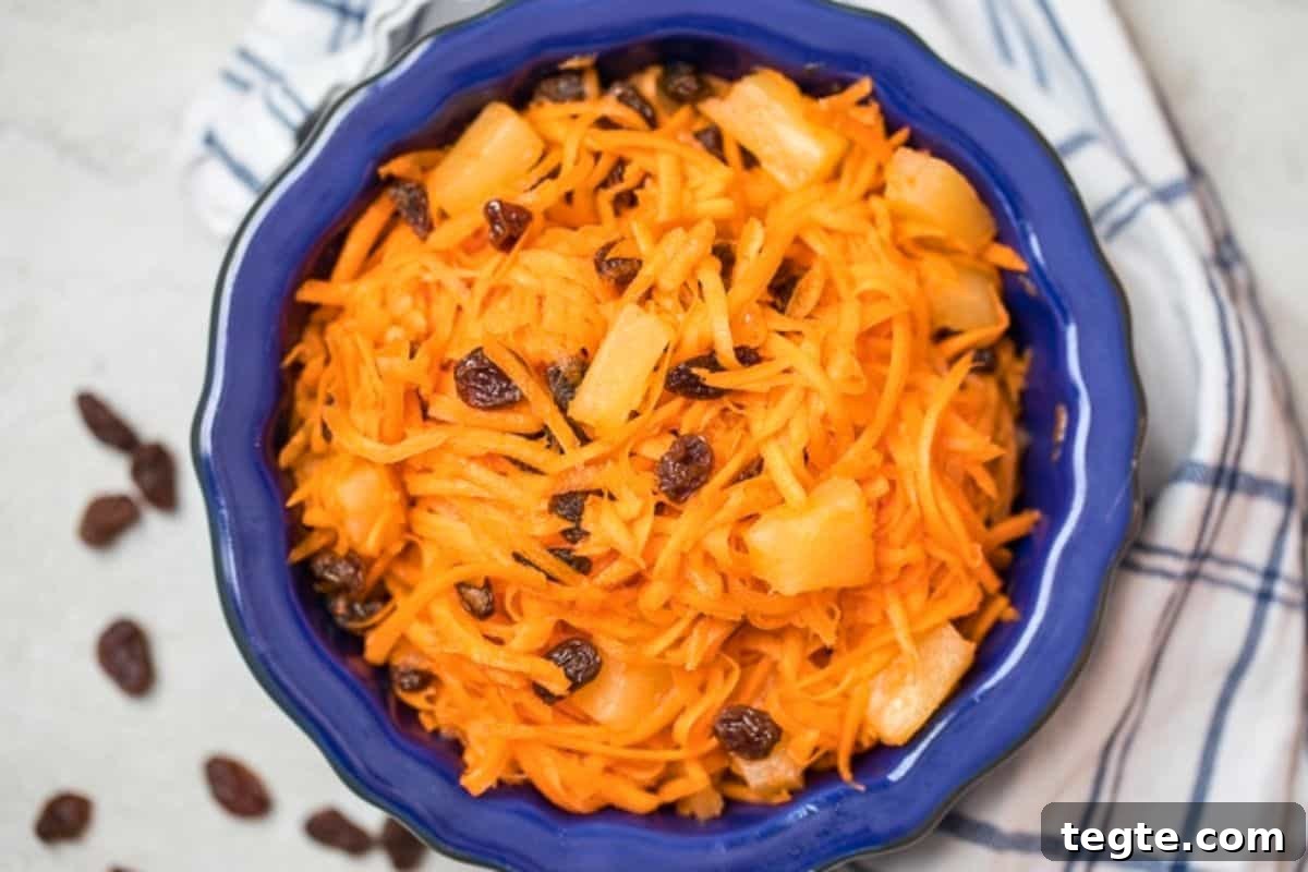 Carrot Raisin Salad No Mayo Shredded carrots tossed with raisins, pineapple, and a sweet dressing in a blue bowl.