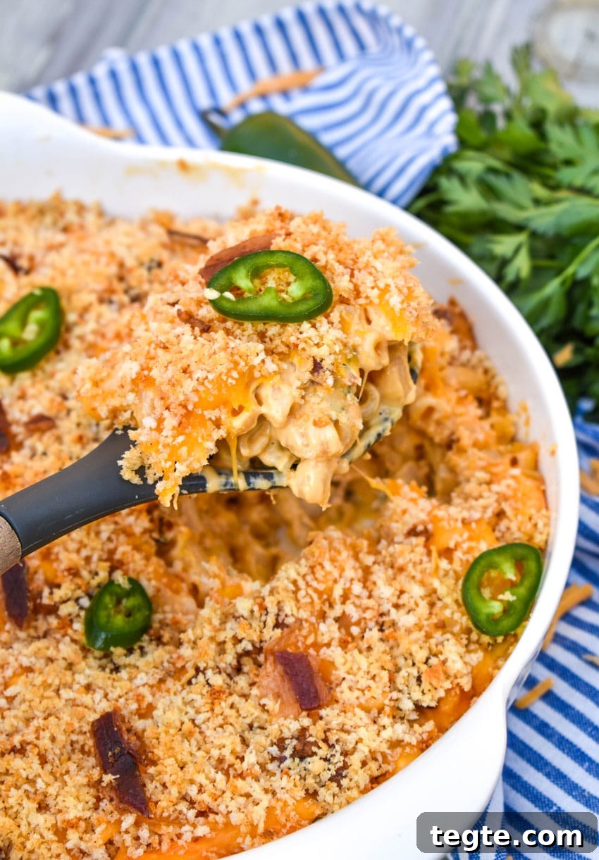 a serving spoon scooping jalapeno popper mac and cheese out of a large white serving bowl