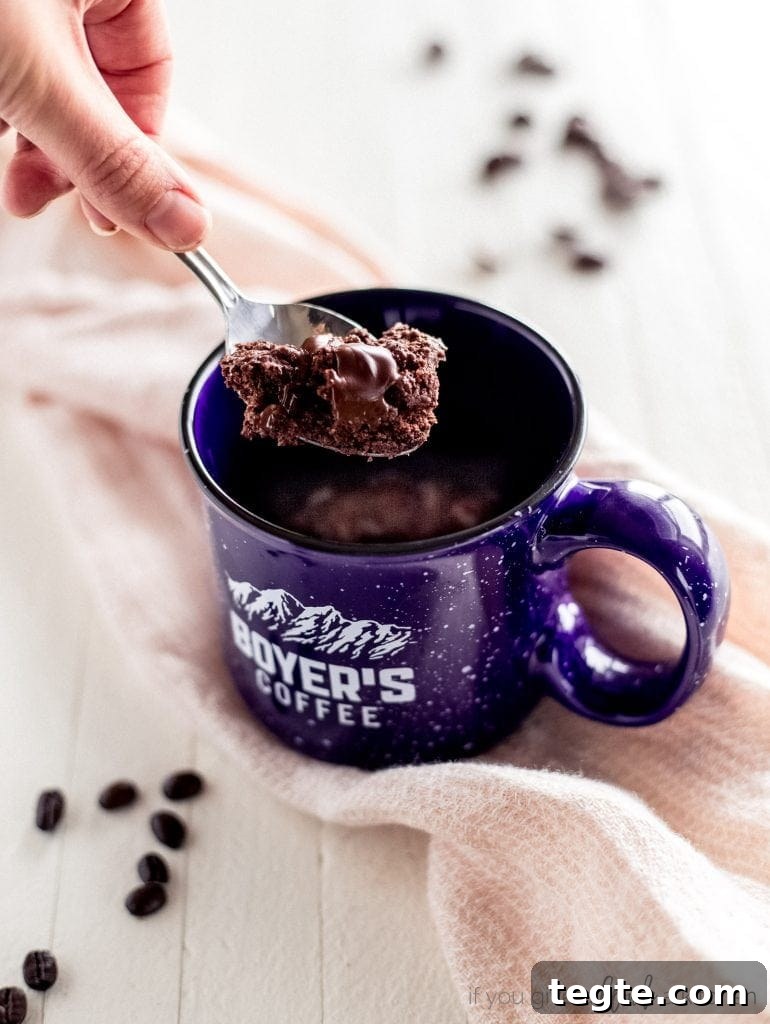 Microwave Double Chocolate Chip Mug Cookie Recipe 2 hand holding spoon with double chocolate chip cookie. Blue mug with cookie inside
