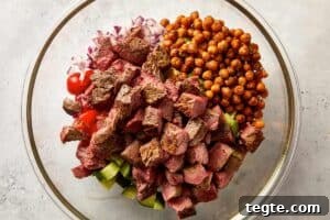 Add the cherry tomatoes, cucumber, red onion, avocado, roasted chickpeas and cubed steak to a large bowl.