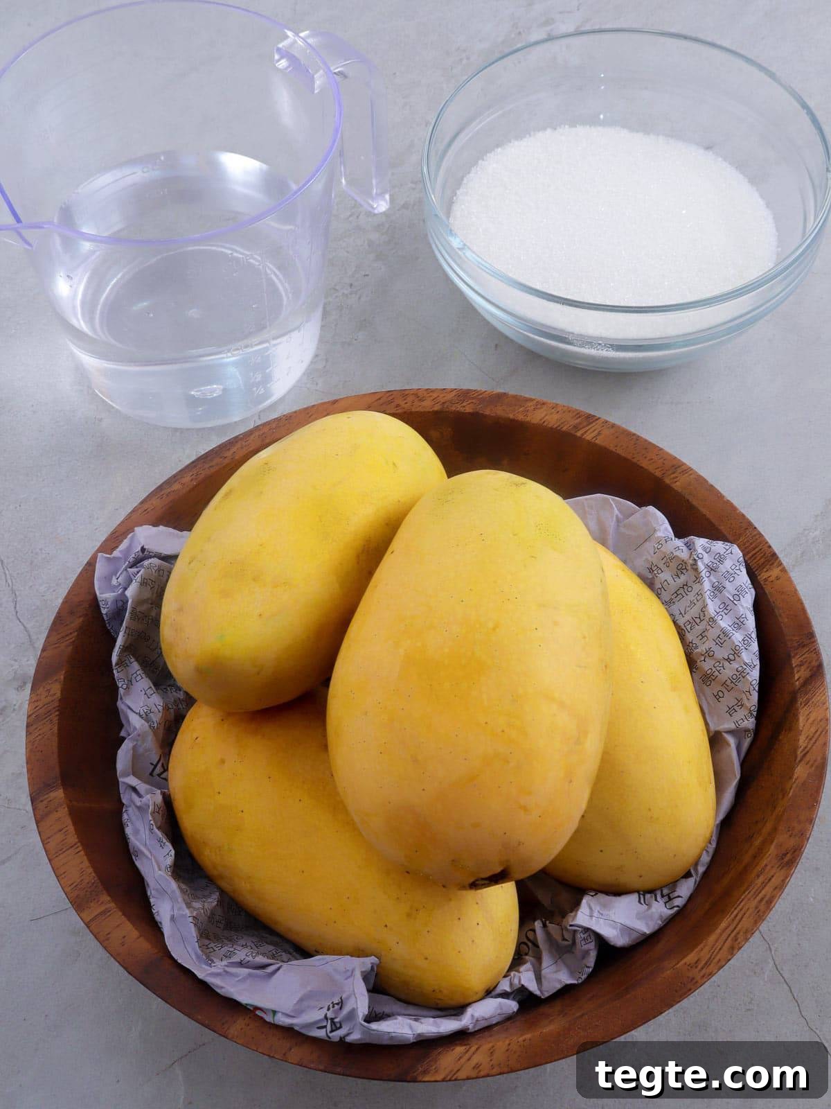 Homemade Mango Nectar Recipe: Smooth, Fresh Mango Drink 3 Manila mangoes in a brown bowl with a a glass of water and a bowl of sugar on the side