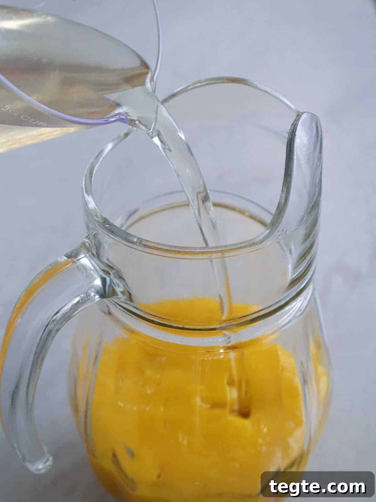 Homemade Mango Nectar Recipe: Smooth, Fresh Mango Drink 7 adding simple to mango pulp in a glass pitcher