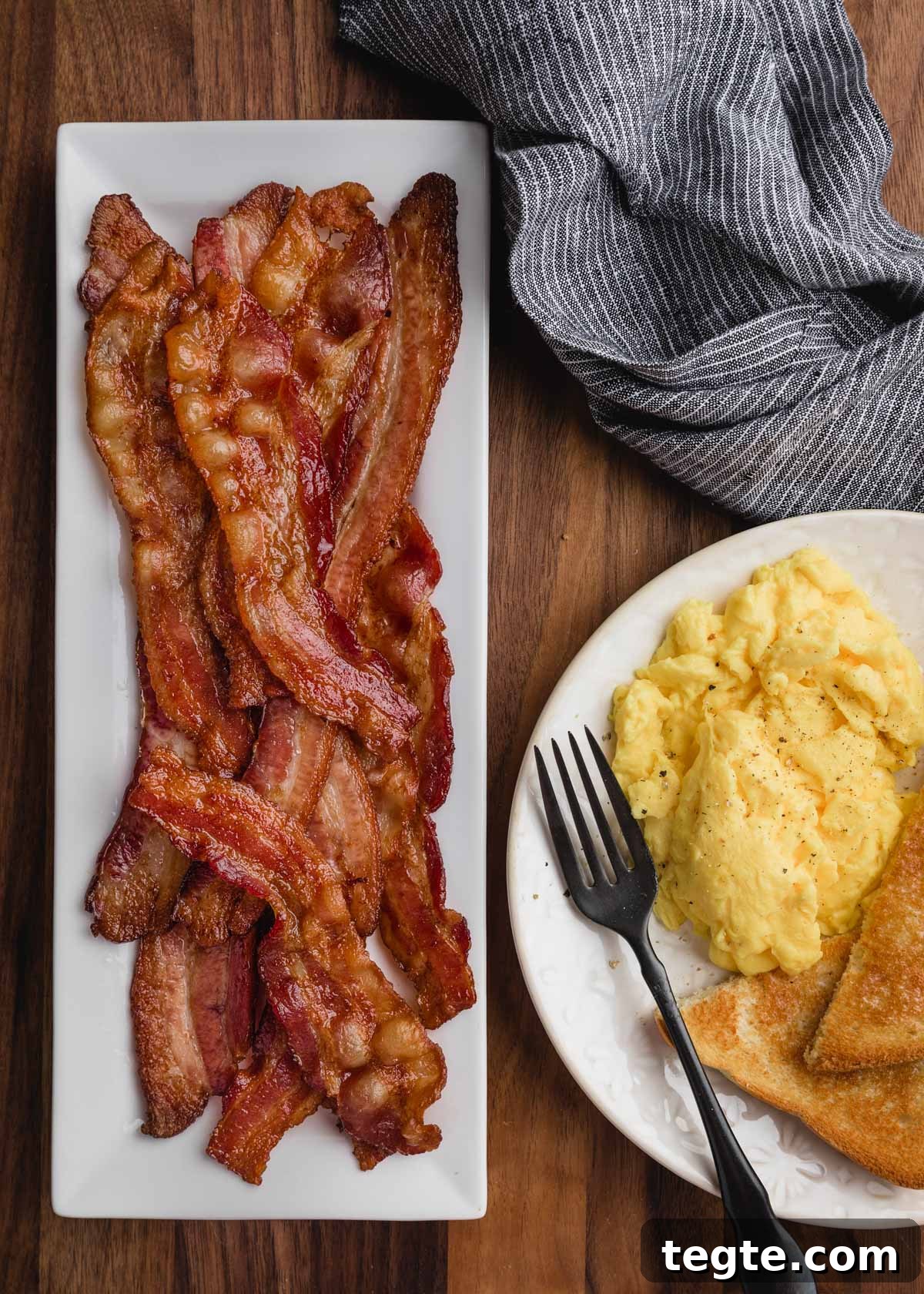 overhead of bacon on a white rectangular platter with a breakfast plate of eggs on the side