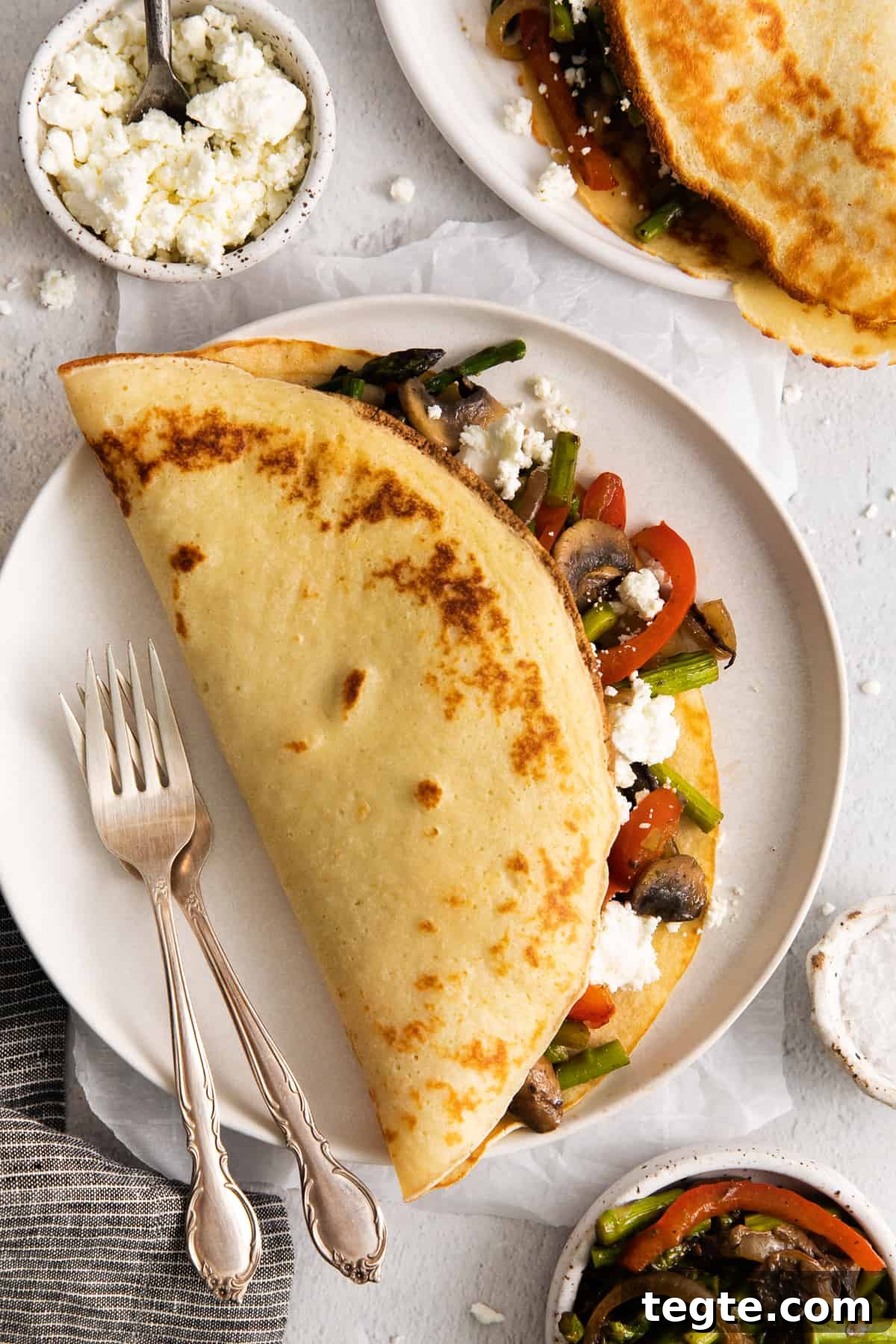 These goat cheese crepes are easy to make, and have a creamy goat cheese filling. Make the crepe batter, sauté veggies, and throw it all together in one skillet! Goat cheese crepe on a plate with a fork.