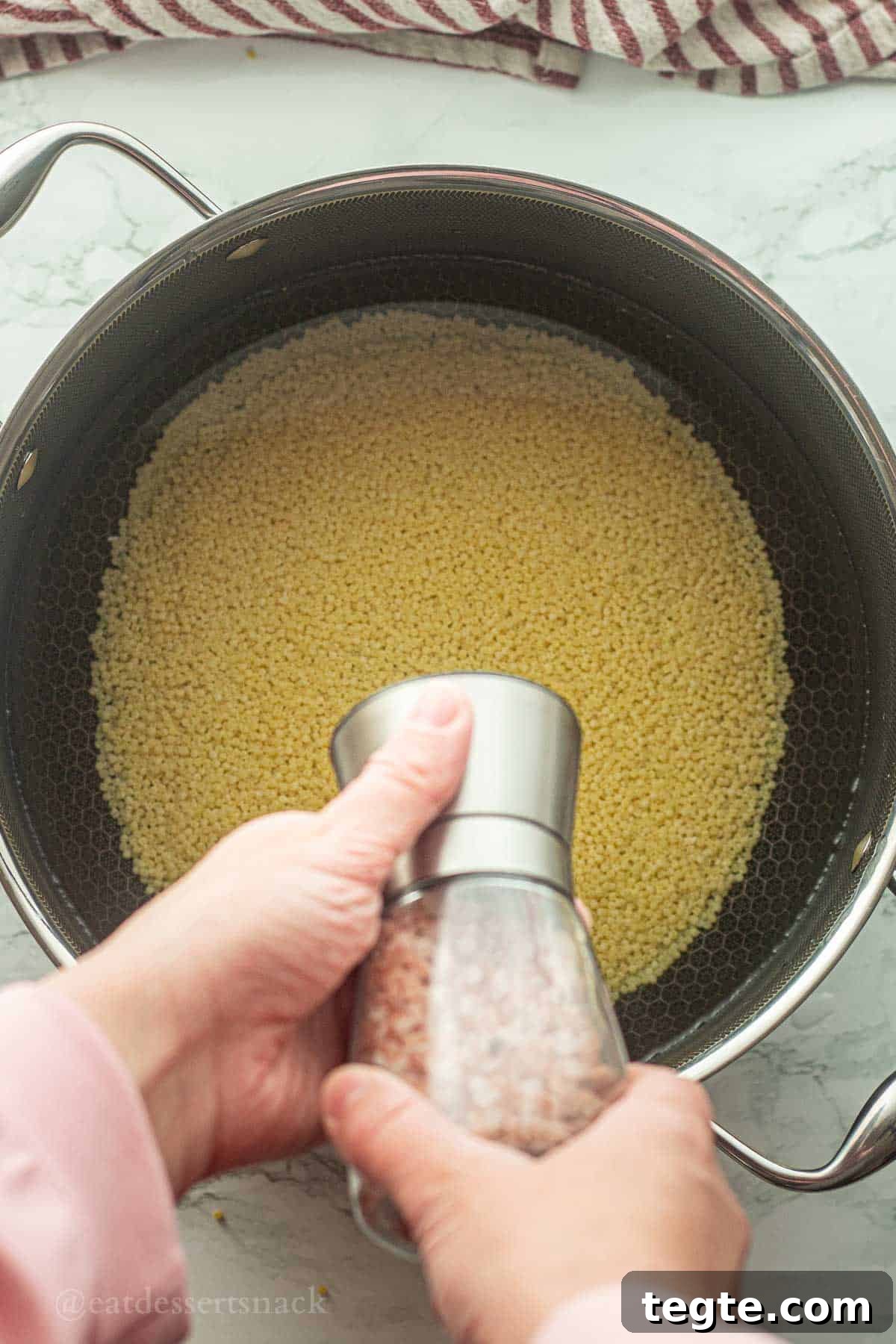 Salt shaker above pot of uncooked acini de pepe noodles.