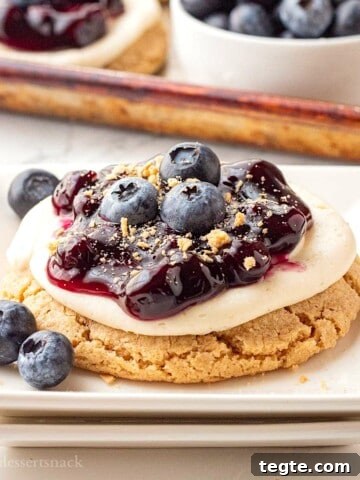 Blueberry pie filling on top of cheesecake cookie on white plate.