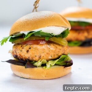 Crispy Salmon Burgers with Lemon-Dill Sauce 12 salmon burger with bun and lettuce on white background.