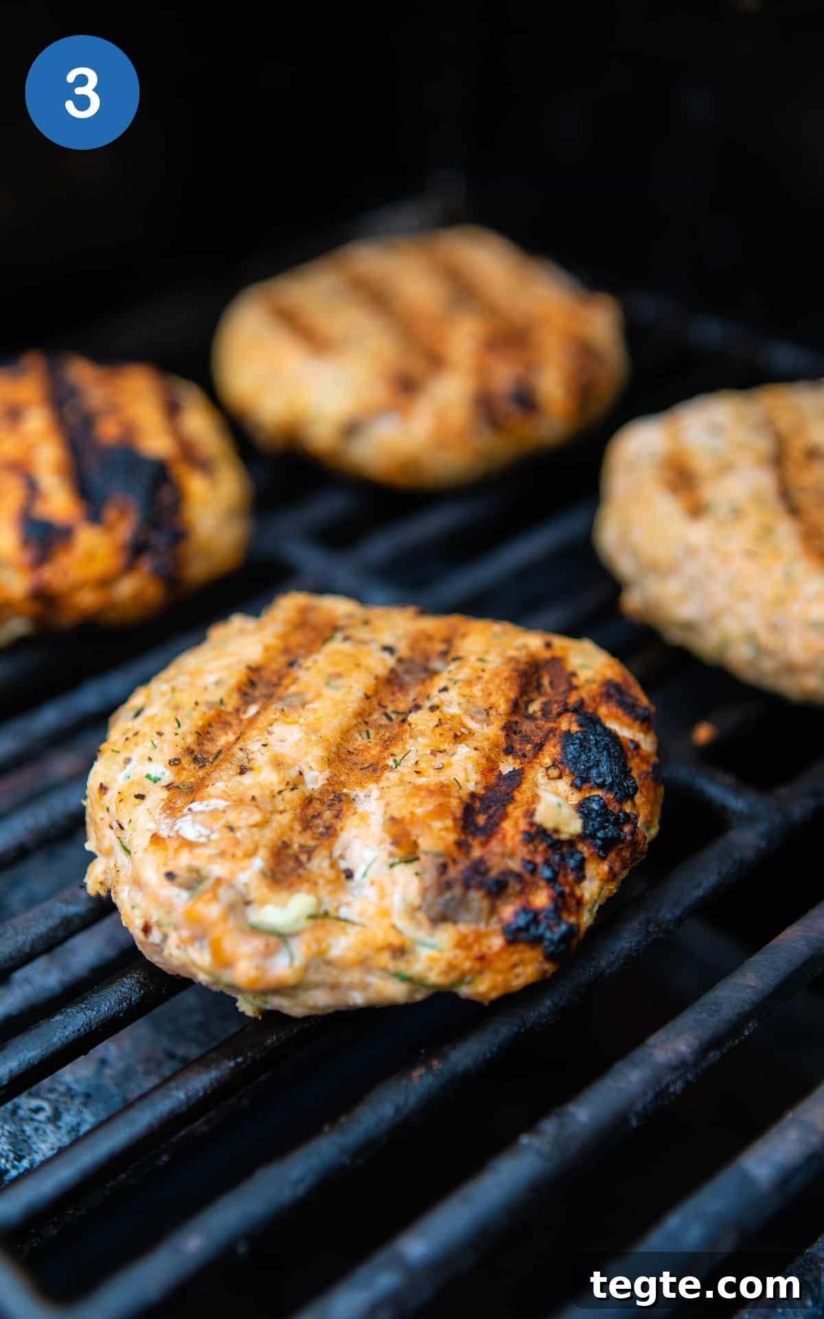 Crispy Salmon Burgers with Lemon-Dill Sauce 6 salmon burgers cooking on black bbq.