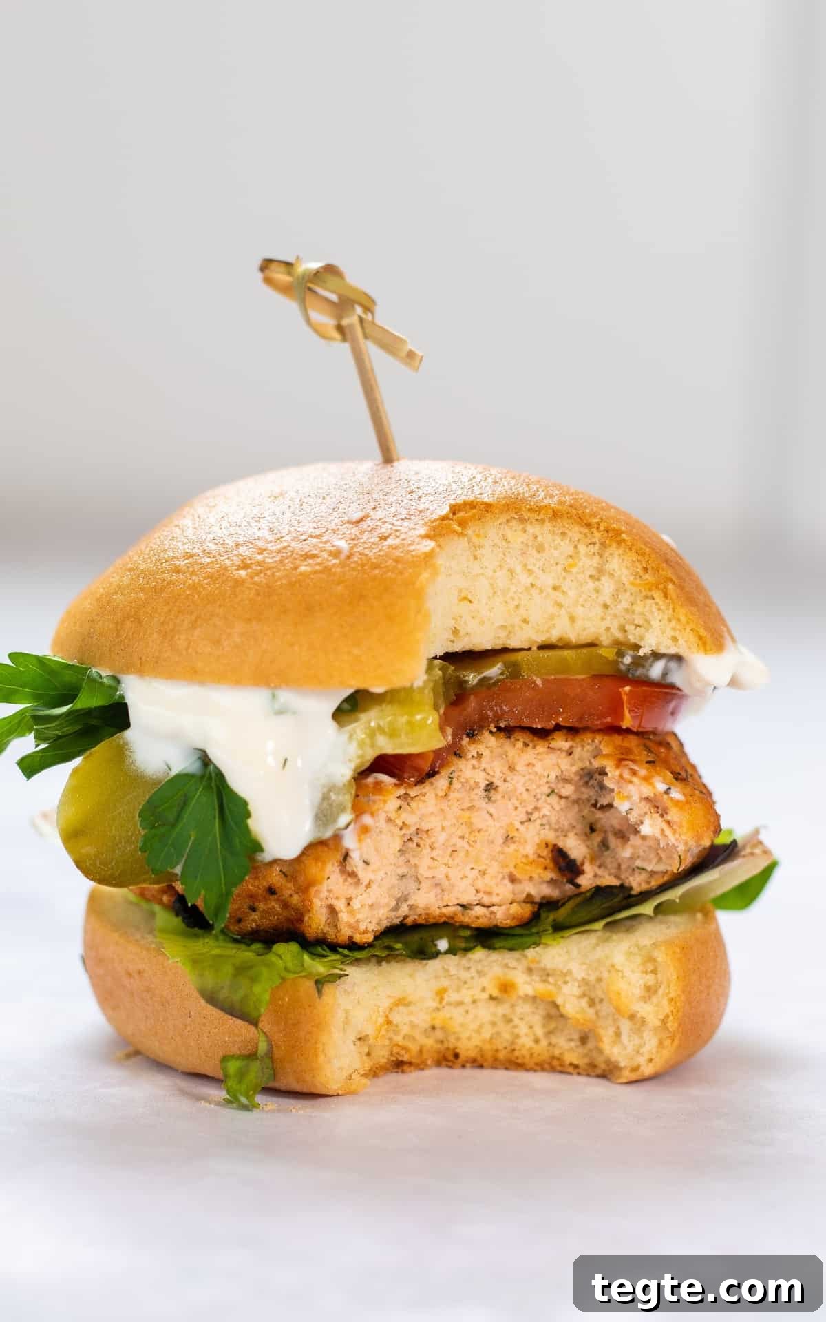 Crispy Salmon Burgers with Lemon-Dill Sauce 7 salmon burgers with bun and lettuce. Bite has been taken from the salmon burger.