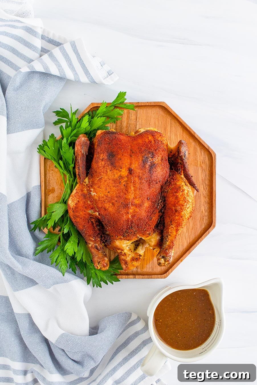 cooked whole chicken on a cutting board with gravy on the side.