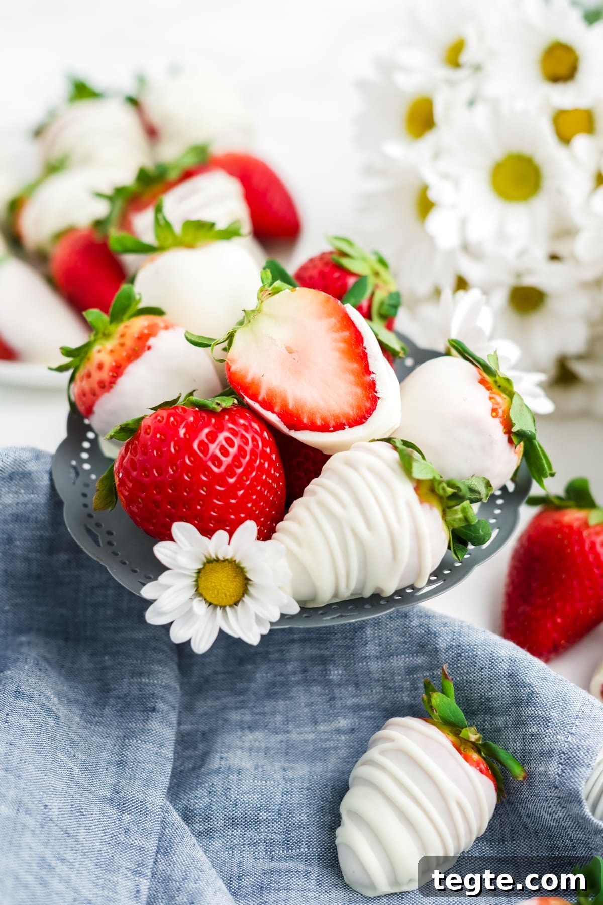 White Chocolate Dipped Strawberries You Can Make at Home 2 A stack of white chocolate covered strawberries on a little platter with one strawberry cut in half.