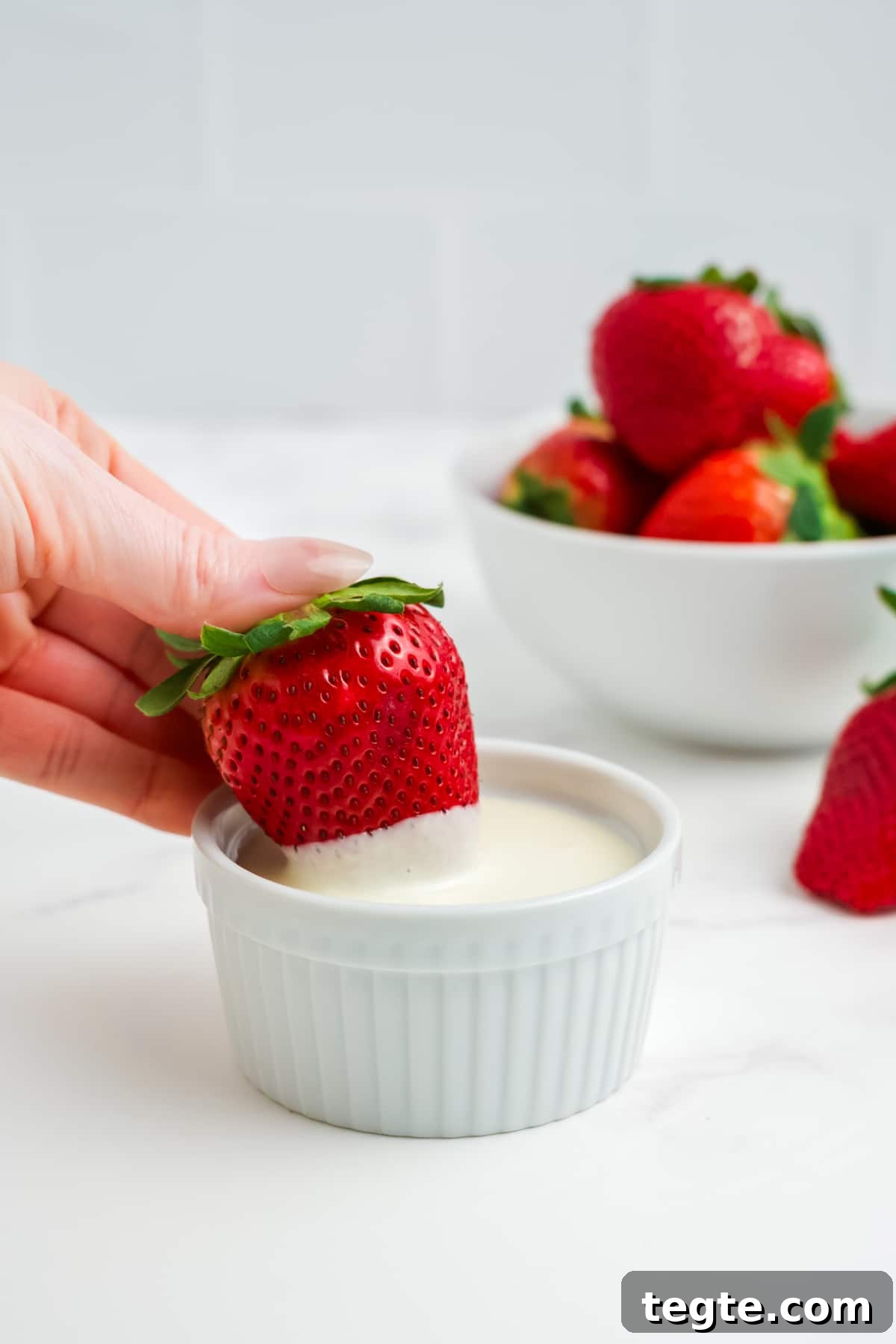 White Chocolate Dipped Strawberries You Can Make at Home 4 A strawberry being dipped into white chocolate.