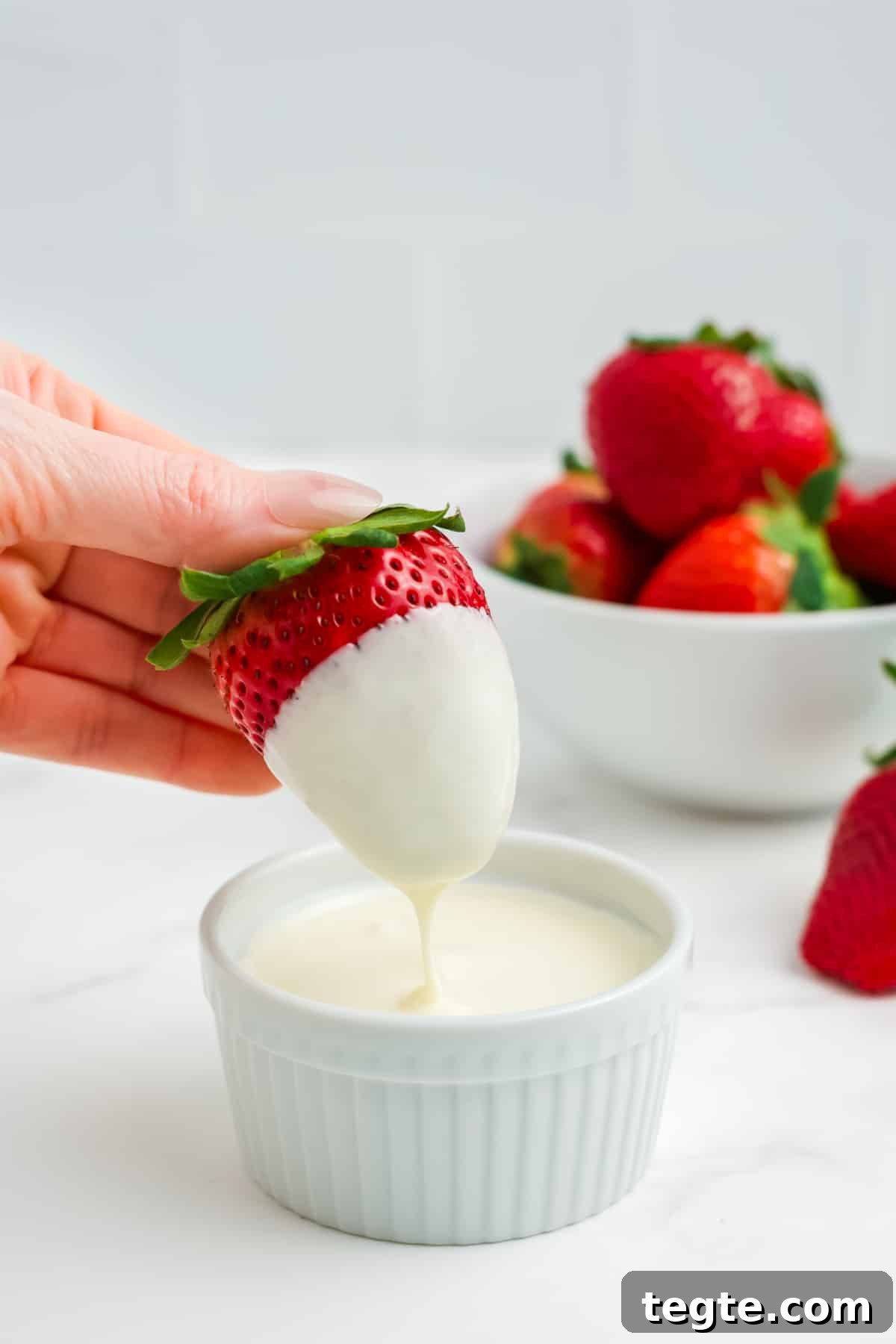 White Chocolate Dipped Strawberries You Can Make at Home 5 A strawberry dripping white chocolate after being dipped.