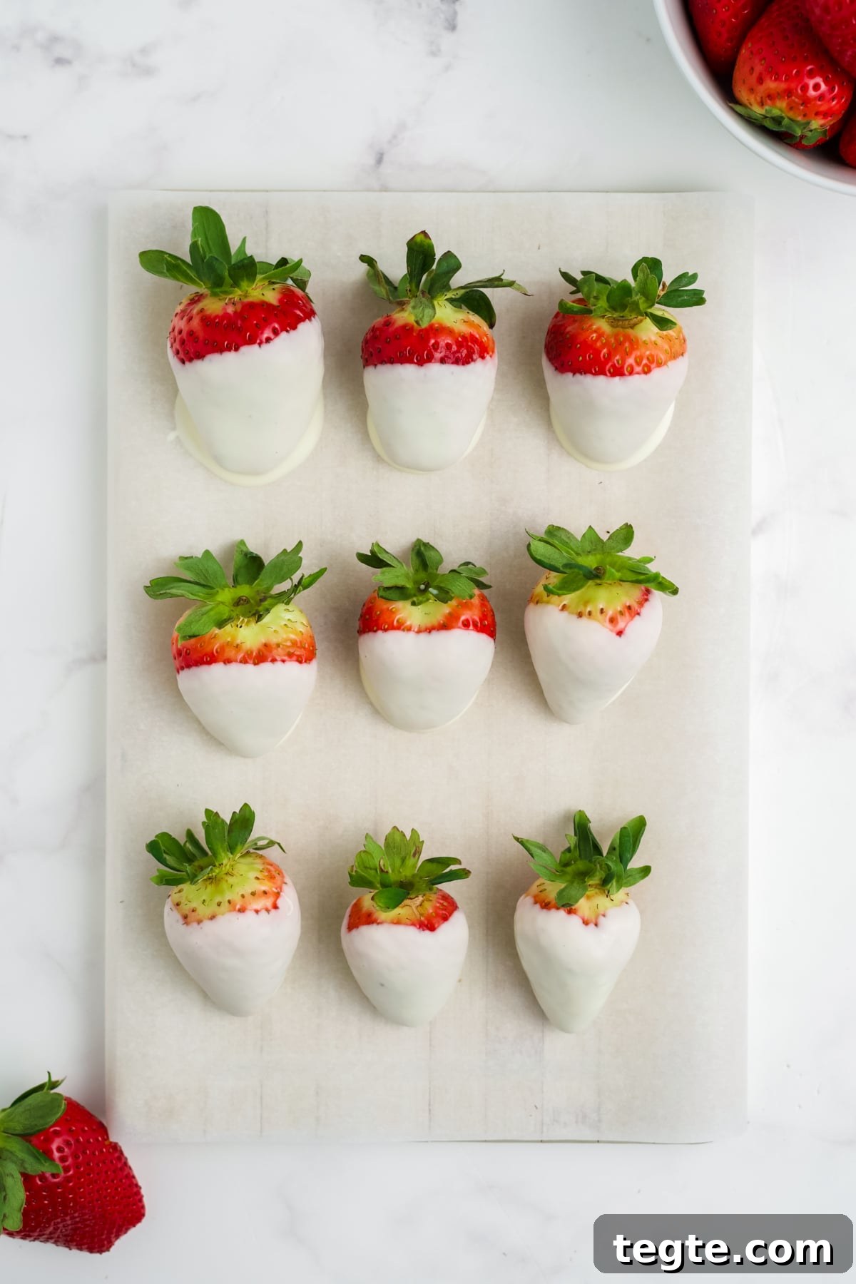White Chocolate Dipped Strawberries You Can Make at Home 6 An overhead image of 9 white chocolate strawberries on parchment paper.