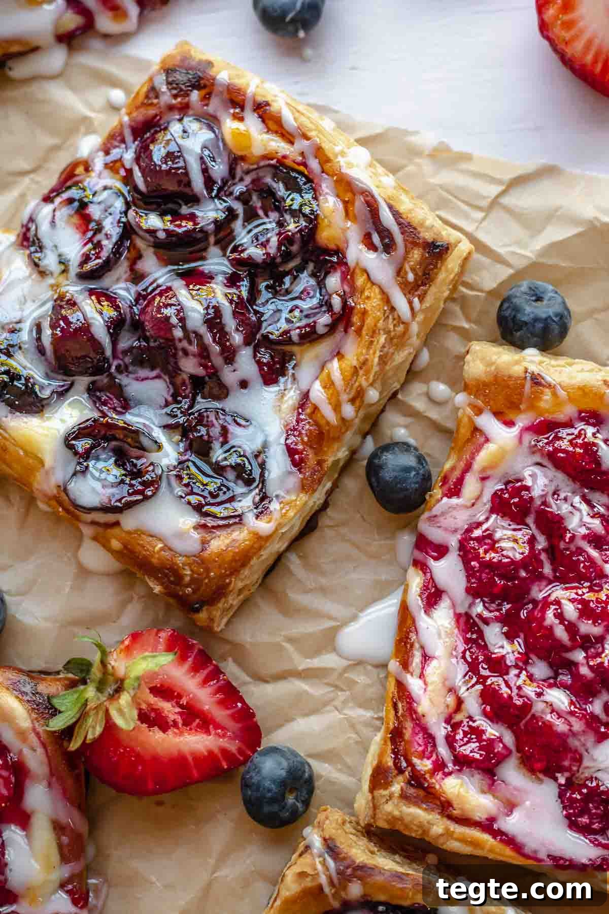 Fruit and Cream Cheese Danish with Flaky Puff Pastry 13 Cherry danish and raspberry cream cheese danish on parchment paper drizzled with icing.
