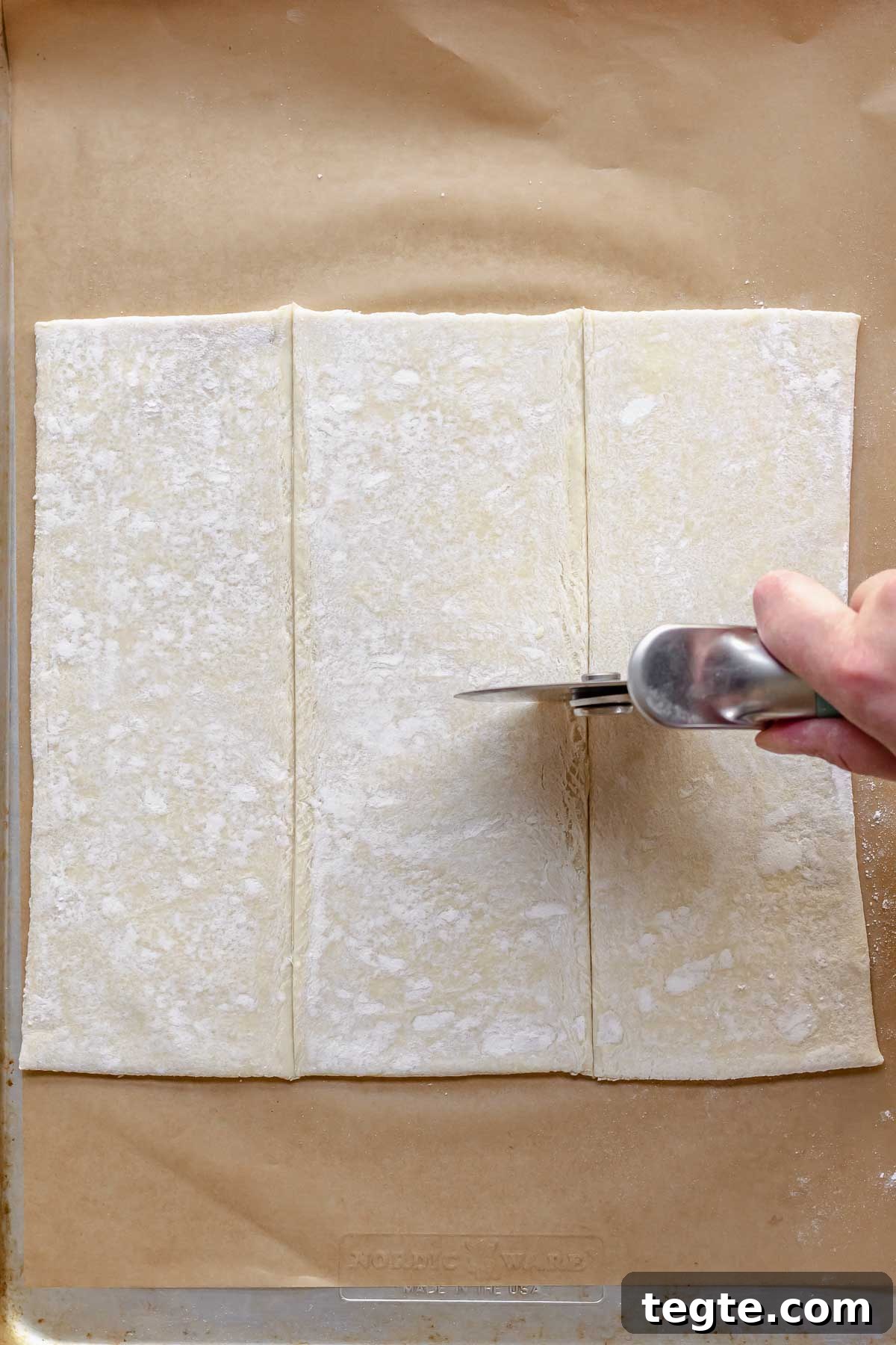 Fruit and Cream Cheese Danish with Flaky Puff Pastry 6 A hand cuts puff pastry into 6 pieces with a pizza cutter.
