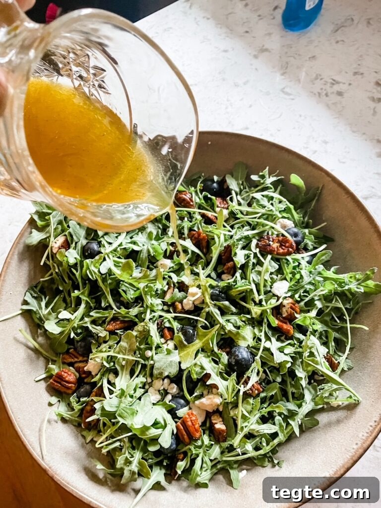 The dressing being poured into the Summer Arugula, Feta, and Blueberry Salad