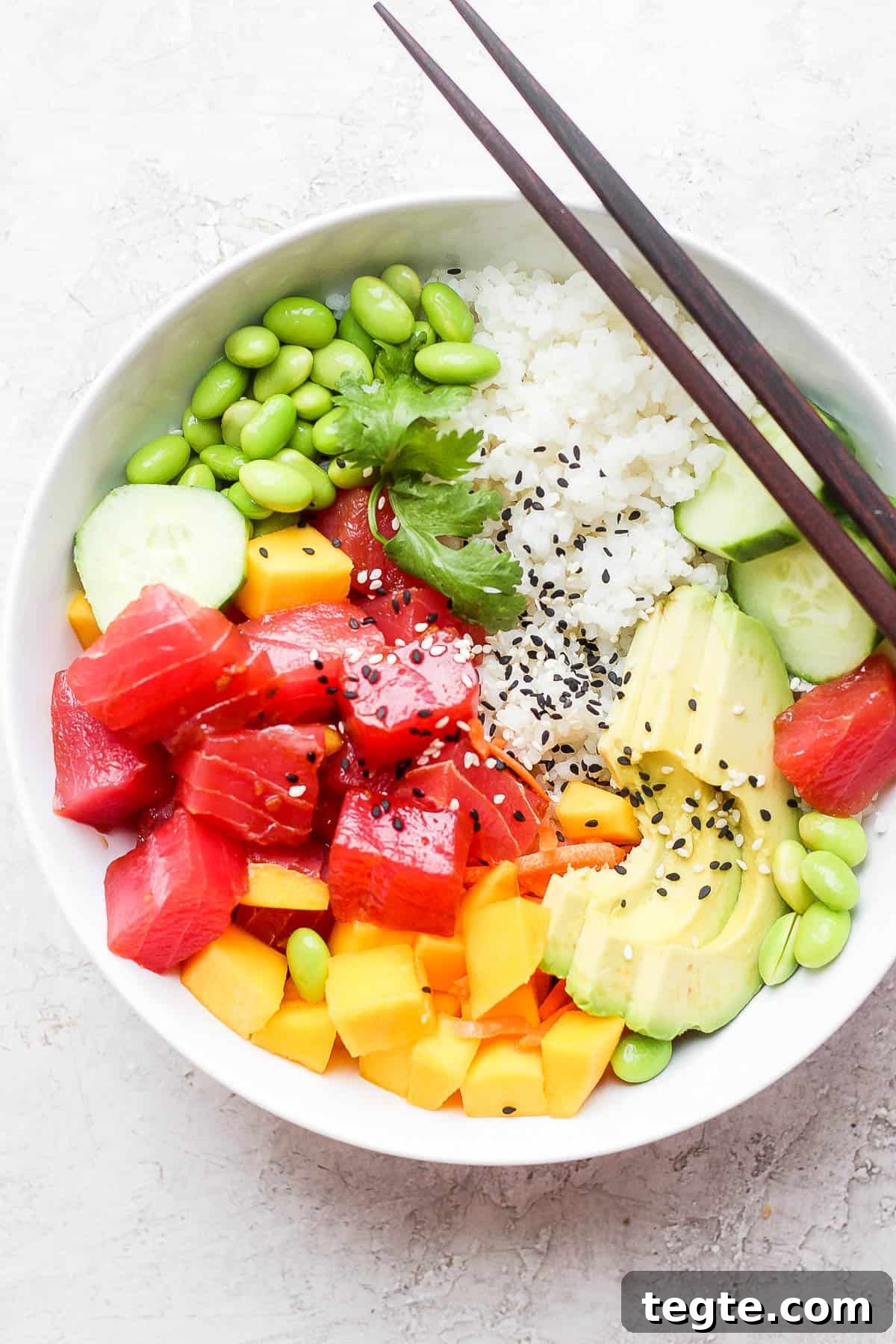 Fresh Tuna Poke Bowl Recipe: Quick Hawaiian-Style Lunch 2 Tuna poke bowl with sushi rice, edamame, cucumber, mango, avocado, cilantro, and chopsticks on the side.