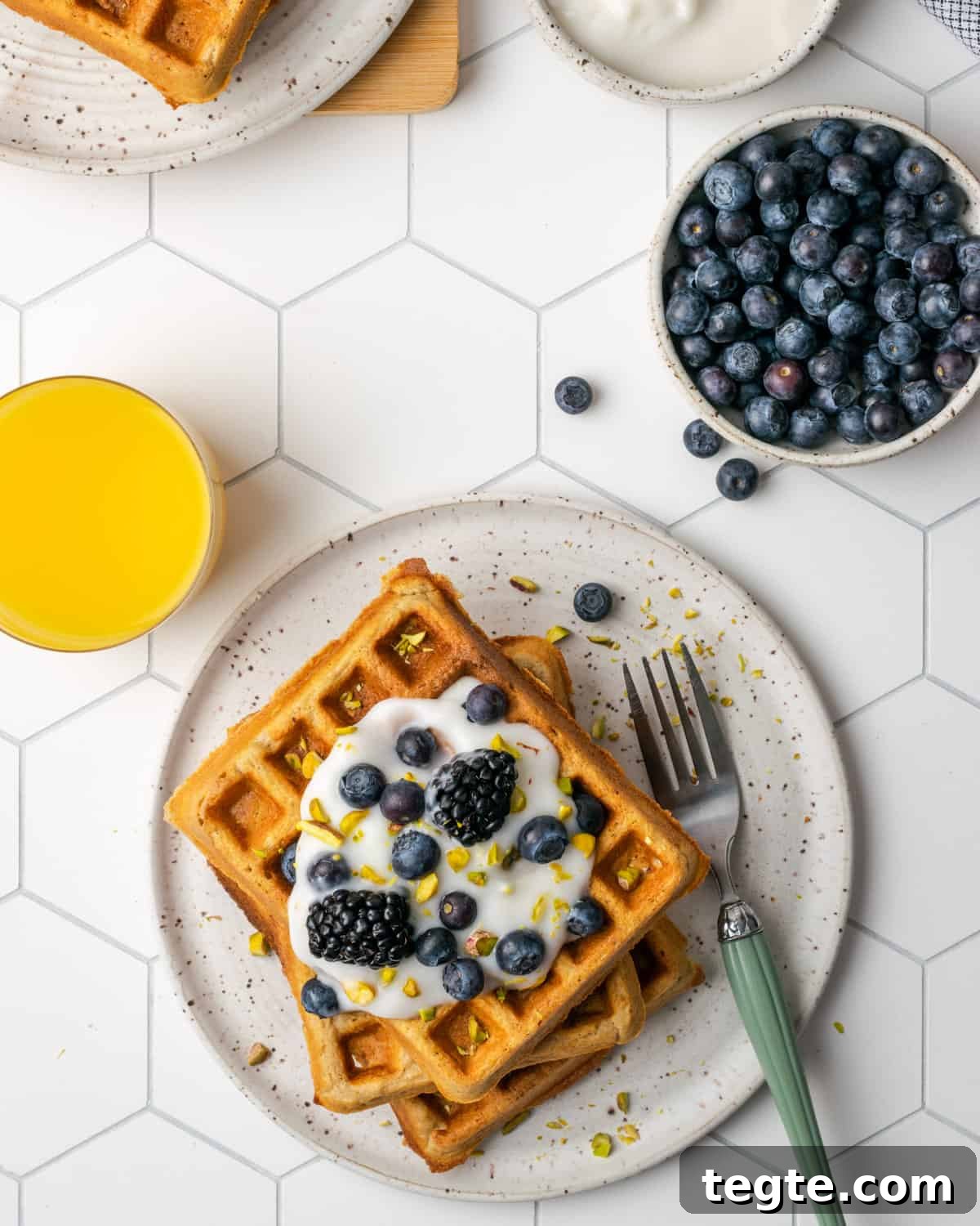Crispy Oat Flour Waffles Recipe - Fluffy & Gluten-Free Option 16 A plate of gluten free waffles next to a bowl of blueberries and a glass of orange juice.