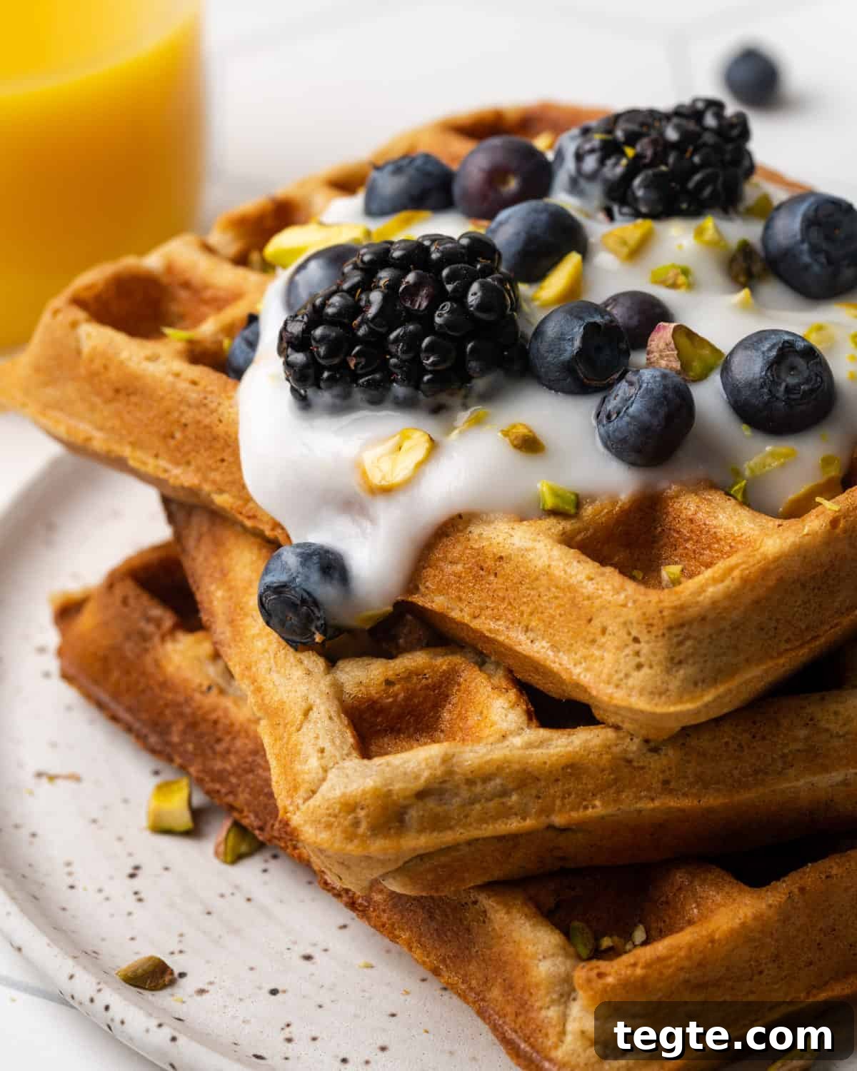 Crispy Oat Flour Waffles Recipe - Fluffy & Gluten-Free Option 17 A closeup of a stack of three oat flour waffles topped with yogurt, blueberries and chopped pistachios.