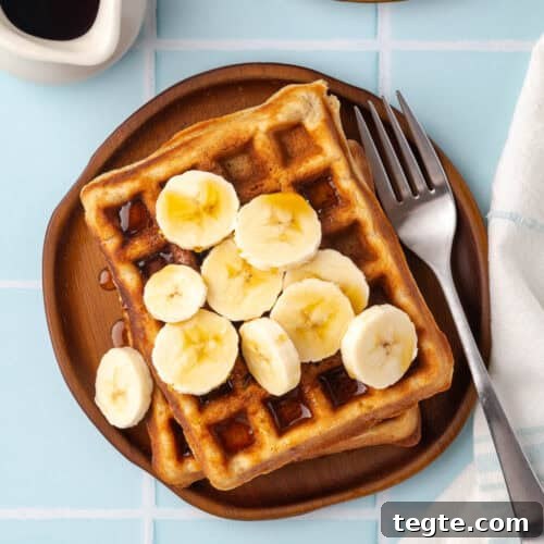 A plate of gluten free banana waffles topped with slices of banana and maple syrup.
