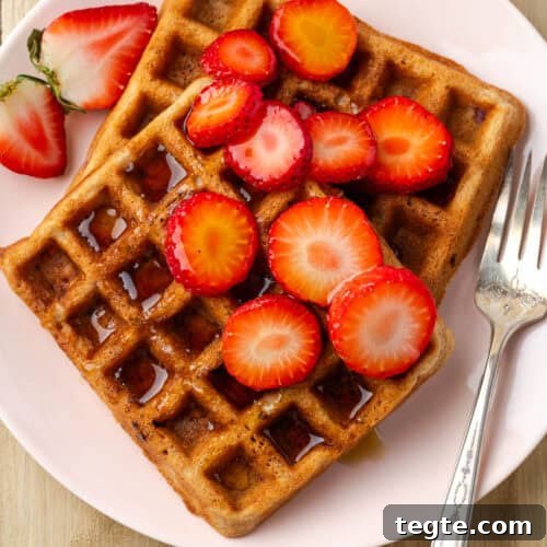 Two strawberry waffles topped with syrup and slices of fresh strawberries.
