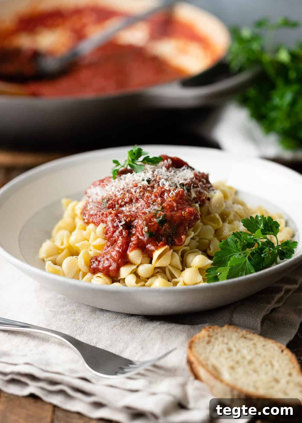 Homemade Marinara Sauce for Spaghetti (Meatless) 3 a white bowl of shell pasta with marinara, cheese, and herbs on top with a piece of bread and a fork visible