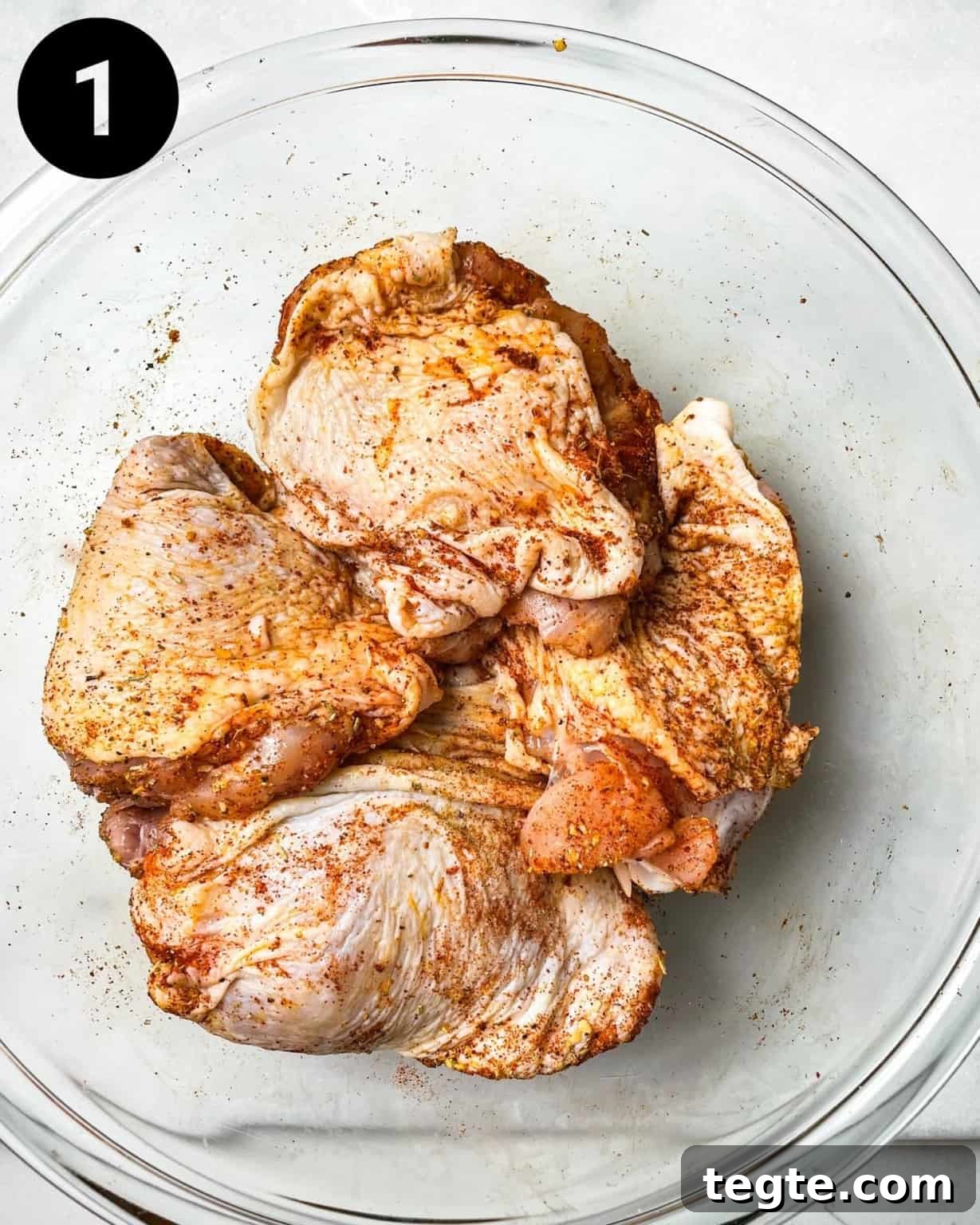 Oven-Baked BBQ Chicken Thighs with Crispy Skin and Sticky Glaze 4 chicken thighs in a bowl coated with seasonings.