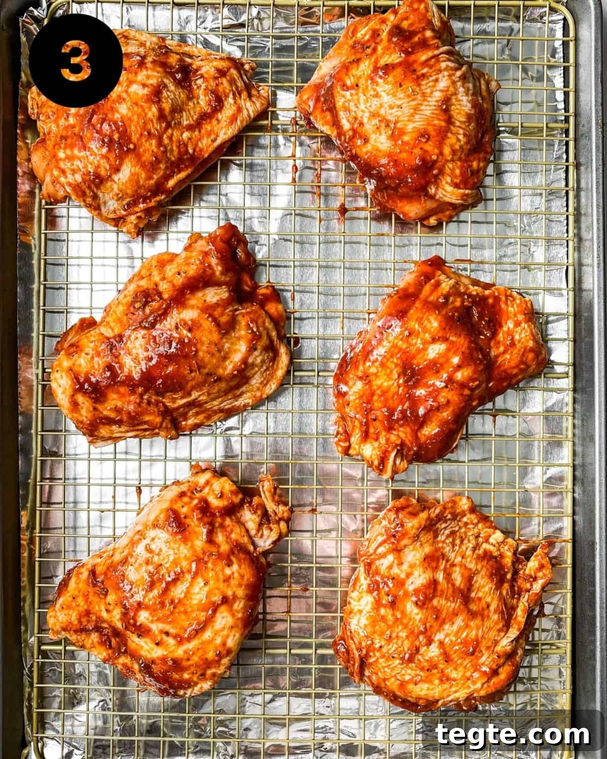 Oven-Baked BBQ Chicken Thighs with Crispy Skin and Sticky Glaze 6 chicken thighs on a sheet pan covered in barbecue sauce.