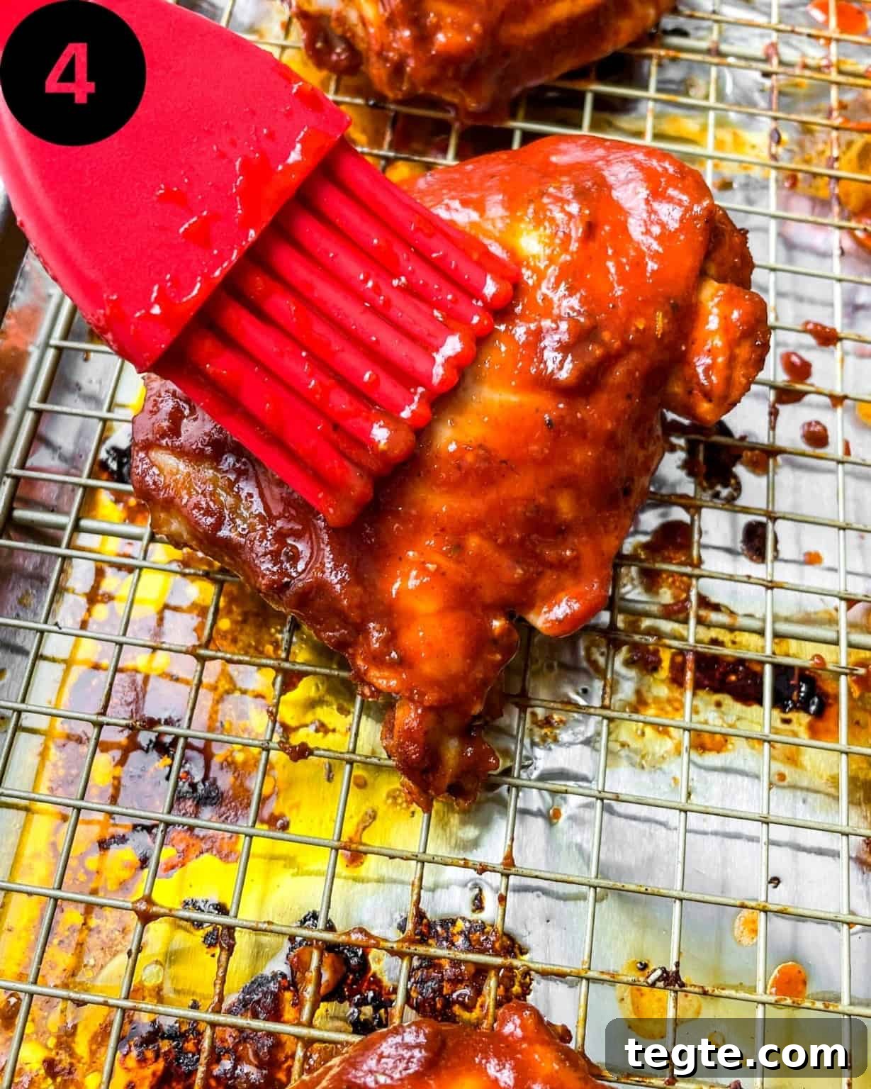 Oven-Baked BBQ Chicken Thighs with Crispy Skin and Sticky Glaze 7 baked bbq chicken thighs on a wire rack with bbq sauce brushed on top.