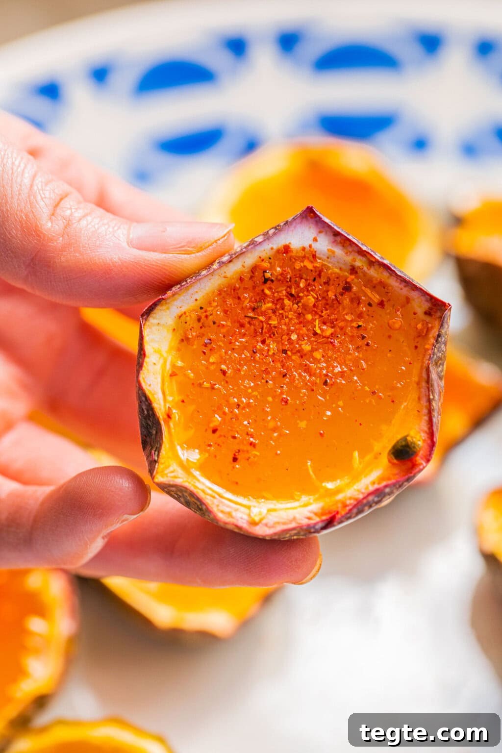 Passion Fruit Tequila Jello Shots Recipe for Parties 8 a hand holding a passion fruit half filled with a jello shot and garnished with tajin