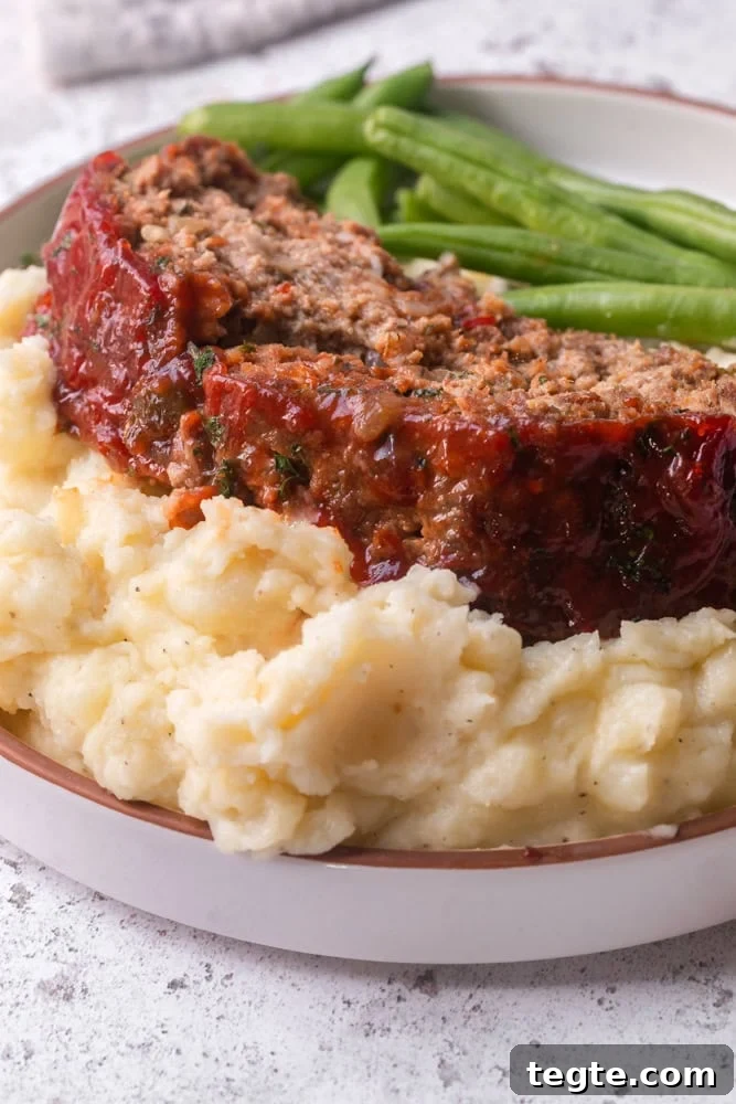 A photo of a thick slice of meatloaf over mashed potatoes on a plate 