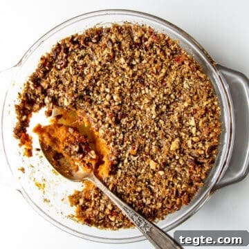 A serving spoonful of sweet potato crunch being taken from a casserole dish.