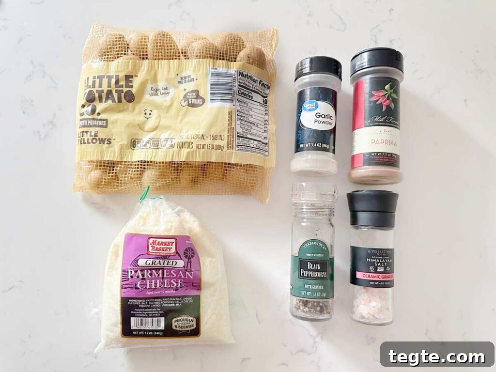 Crispy Air-Fryer Baby Potatoes Recipe 3 baby potatoes, parmesan cheese, garlic powder, paprika, black pepper and salt on a white kitchen counter.