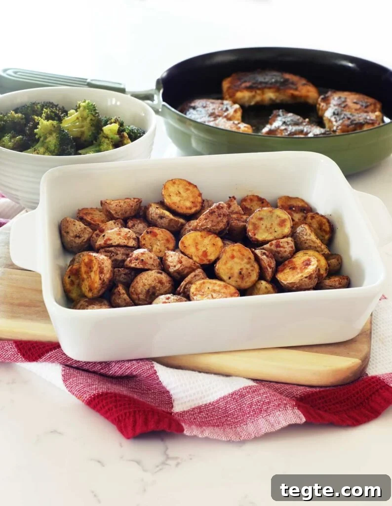 Crispy Air-Fryer Baby Potatoes Recipe 7 A white baking dish of AirFryer Baby Potatoes on a cutting board with cast iron pork chops and broccoli.