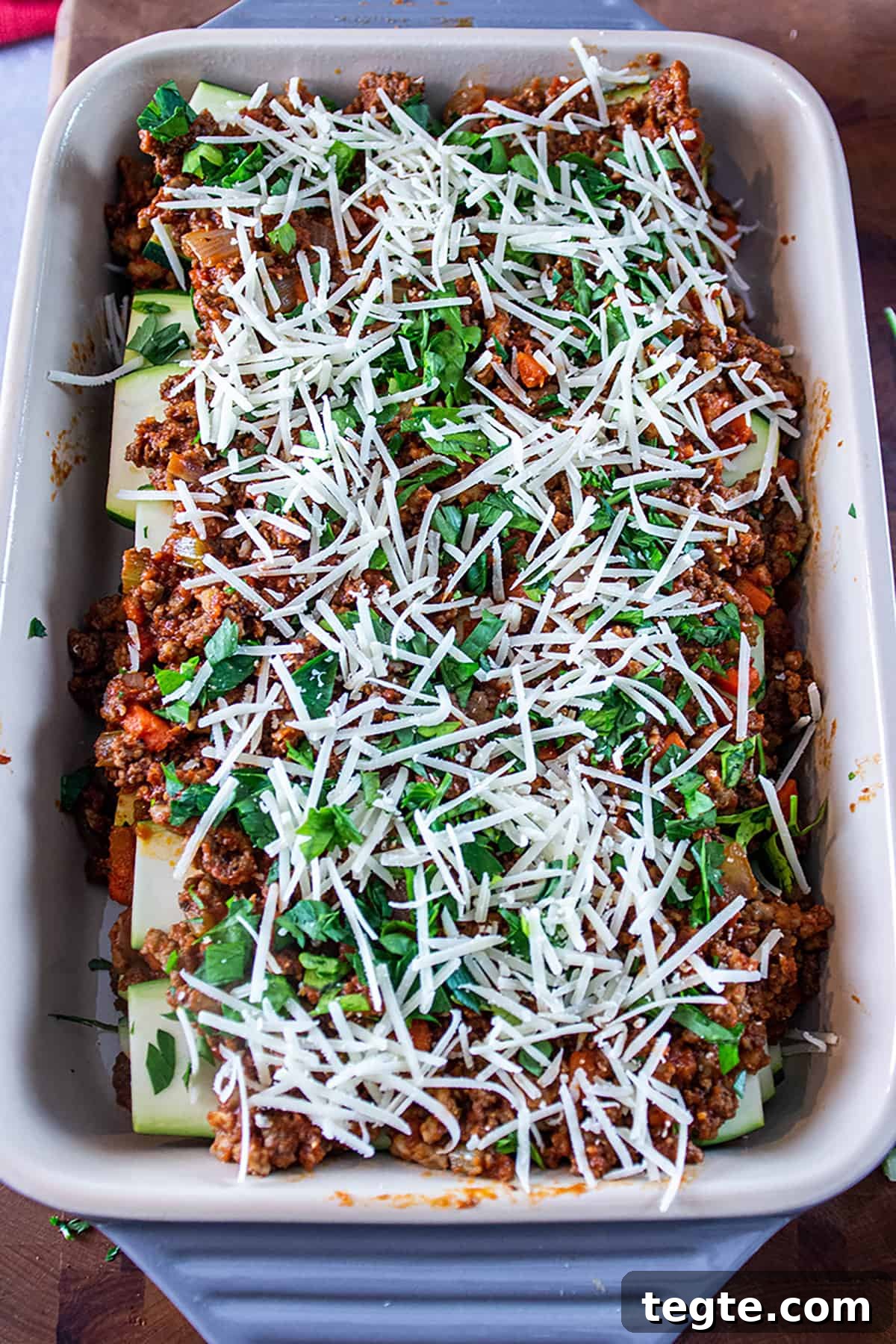 Zucchini Lasagna with Rich Bolognese Meat Sauce 7 Pan filled with a zucchini lasagna topped with parmesan cheese and fresh parsley.