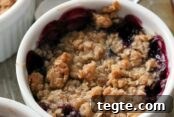 Berry cobbler in a ramekin dish with two spoons faded in the background. On the left side of the photo are partial pictures of two ramekins with berry cobbler. The text Single Serve Berry Cobbler is overlaid on the photo at the top right. Overlaid on the bottom right is the text reallifedinner.com.